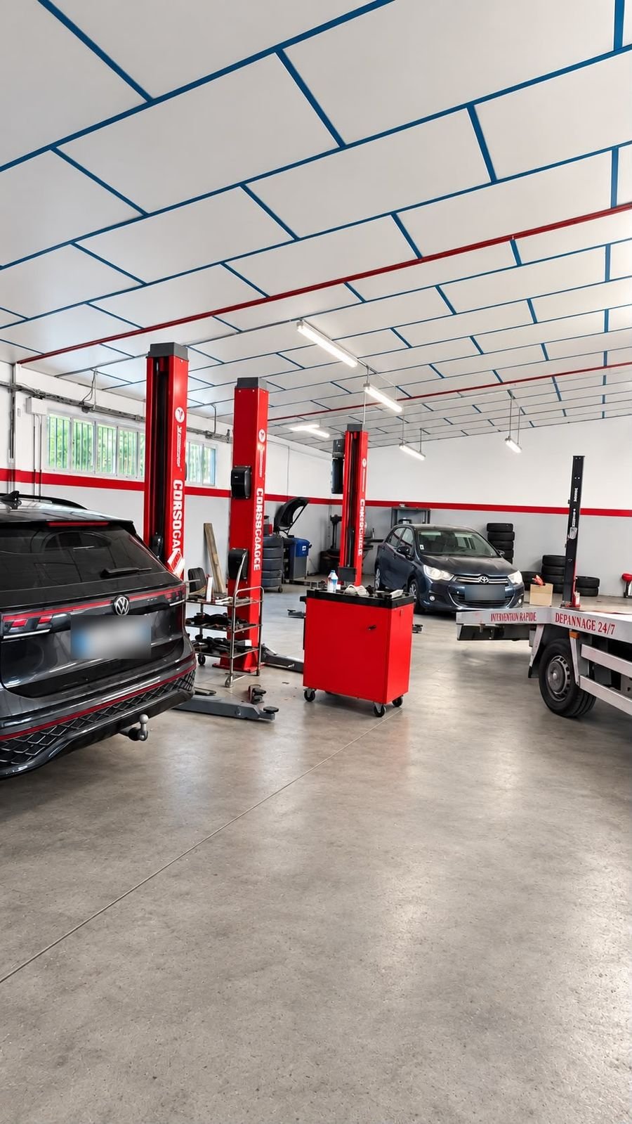 Atelier avec ponts élévateurs rouges, servante d’outils et véhicules
