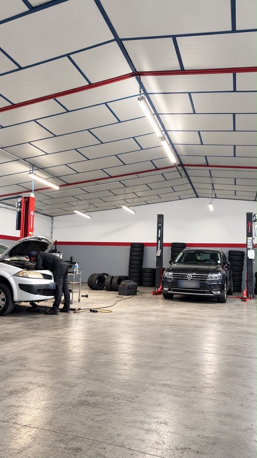 Mécanicien au travail sous le capot d’une voiture, pneus stockés au fond de l’atelier